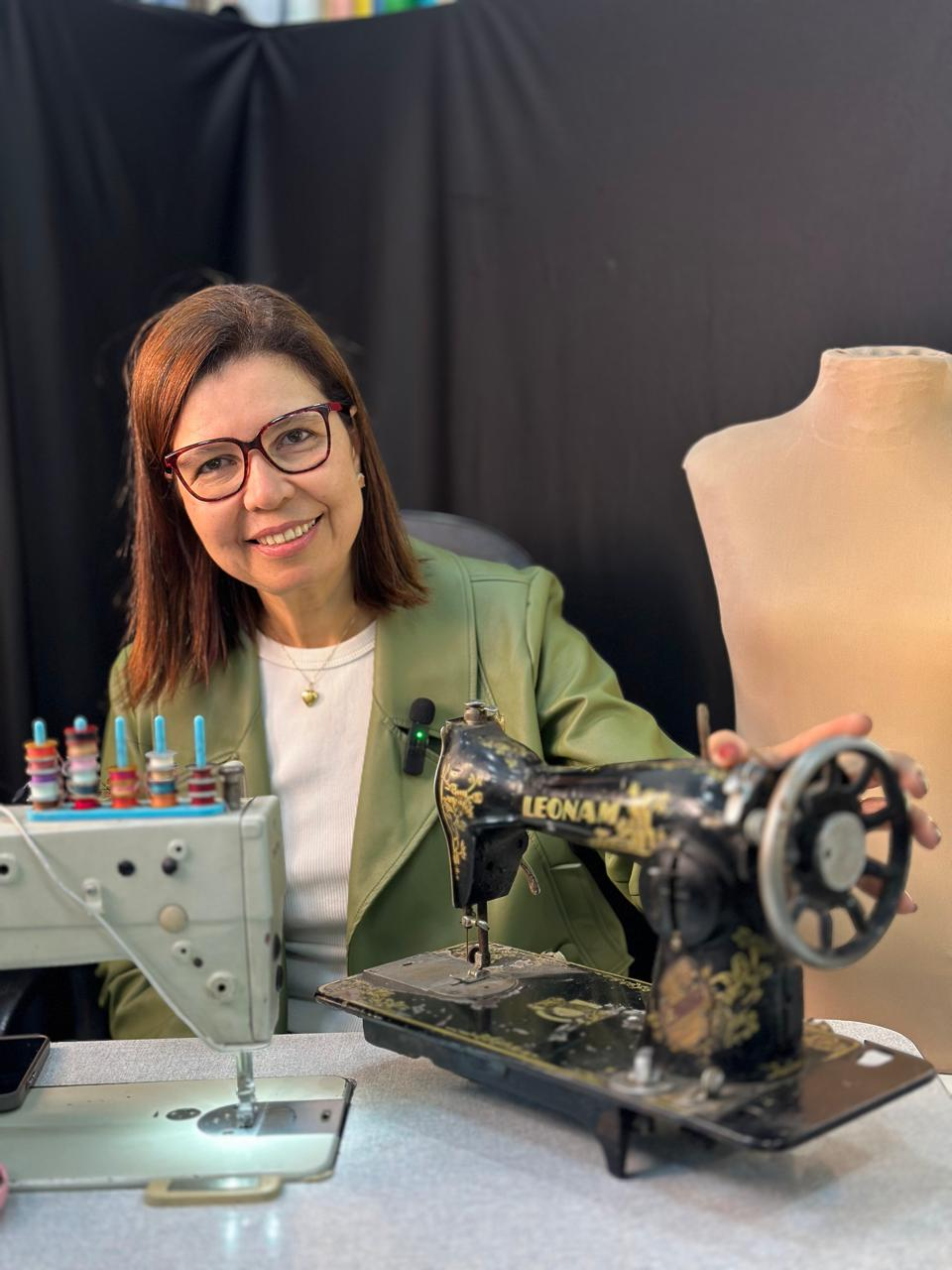Di Almeida em seu ateliê de costura com máquina de costura vintage
